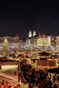 an outdoor christmas market is lit up at night with lights on the trees and buildings in the background