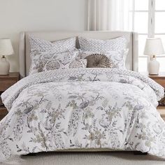 a bed with white and grey comforters in a bedroom next to two lamps on either side of the bed