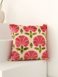 a pink and green pillow sitting on top of a white shelf next to a vase