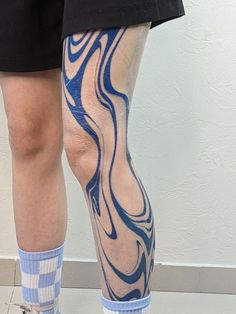 a person with blue and white tattoos on their legs, standing in front of a wall