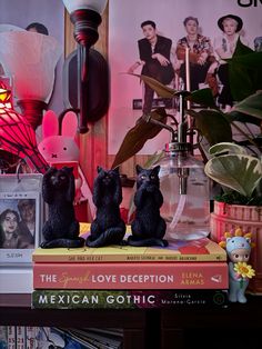 three black cat figurines sitting on top of books in front of a lamp