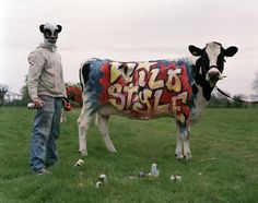 a man standing next to a cow with graffiti on it's body in a field