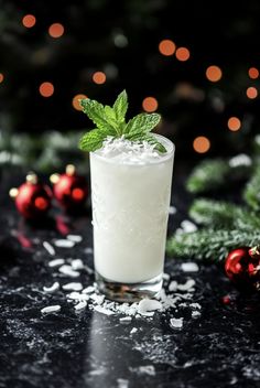 a tall glass filled with white liquid and topped with a green leaf, surrounded by christmas decorations