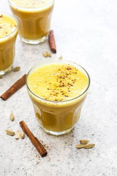 two glasses filled with orange juice and cinnamons next to each other on a table