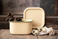 two white dishes with pine cones in them on a wooden table next to an empty dish