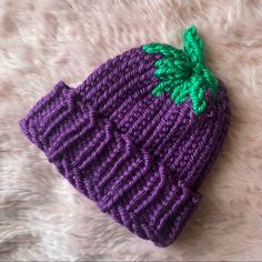 a knitted purple hat with a green leaf on the top sitting on a white furnishing