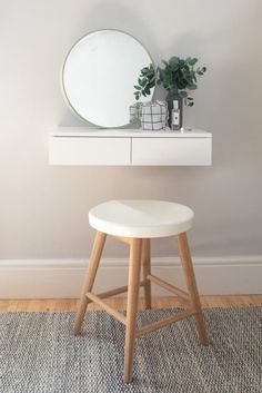 a white stool sitting in front of a mirror on top of a wooden table next to a potted plant