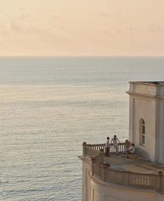 some people are sitting on the ledge of a building by the water and looking out at the ocean