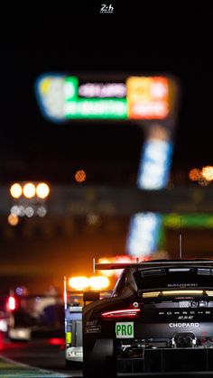 a racing car driving down a race track at night with the lights on in the background