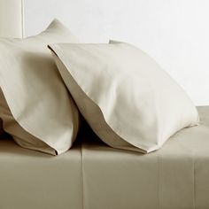 two white pillows sitting on top of a bed next to each other with sheets folded over them