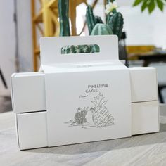 an open white box with a pineapple cake in it sitting on a table next to a potted plant