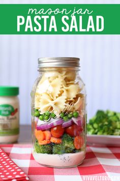 a mason jar filled with pasta salad sitting on top of a checkered table cloth