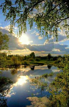 the sun shines brightly through the clouds over a river with trees and grass on both sides