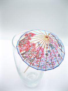 an umbrella is sitting in a glass vase on a white tablecloth with red and blue designs