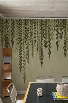 a dining room table with chairs and a wall painted with green leaves hanging from the ceiling