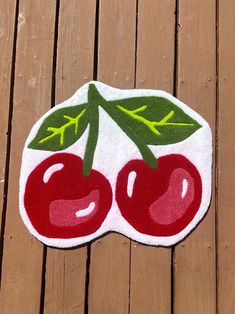 a patch with cherries on it sitting on top of a wooden floor next to a piece of wood