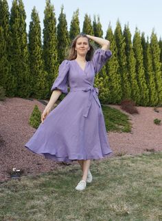 a woman in a purple dress is standing on the grass with her hands behind her head