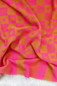 an orange and pink patterned fabric on top of a white blanket with a black cat