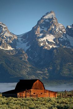 an old barn sits in front of the mountains