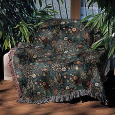 a couch covered in a blanket sitting on top of a wooden floor next to a potted plant