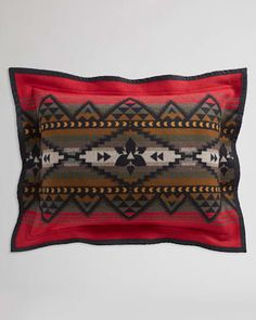 a red and black pillow with an arrow design on the front, sitting against a white wall