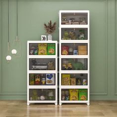 a white book shelf filled with books on top of a hard wood floor next to a green wall