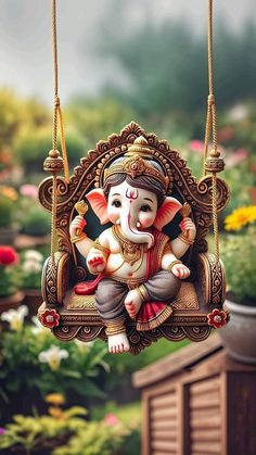 an elephant statue hanging from a swing in front of flowers and bushes, with the image of ganesh on it's back