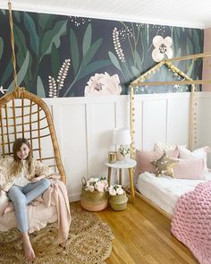 a woman sitting on a chair in a room with flowers painted on the wall behind her