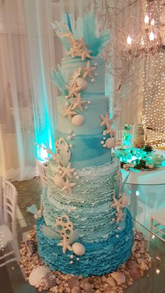 a blue and white wedding cake with seashells on the top is surrounded by sea shells