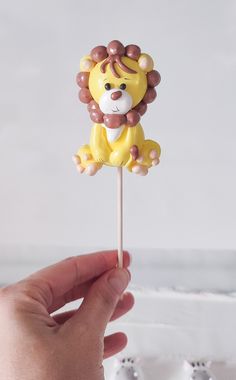 a hand holding a lollipop with a yellow lion on it's head