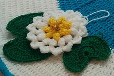 a crocheted flower is on top of a blue and white blanket with green leaves