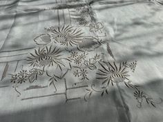 an embroidered tablecloth with flowers and leaves is shown on a bed sheet that appears to be made from linen