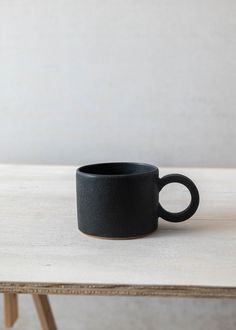 a black coffee cup sitting on top of a wooden table next to a white wall