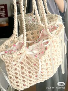 a crocheted bag with bows hanging from it's side and another handbag in the background