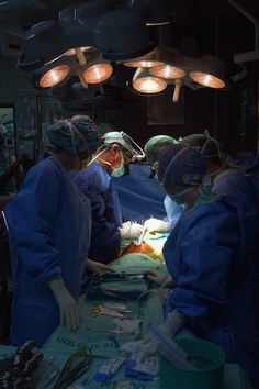 doctors performing surgery in an operating room with lights on above their heads and surgical equipment hanging from the ceiling