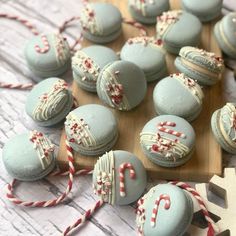 some blue macaroons with candy canes on a wooden board next to other macaroons