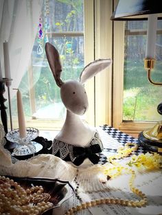 a stuffed rabbit sitting on top of a table next to candles and other items in front of a window