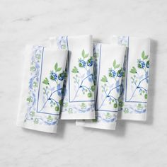 four napkins with blue flowers and green leaves on white marble counter top, set of 4