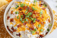 a bowl filled with cheese, bacon and green onions next to some tortilla chips