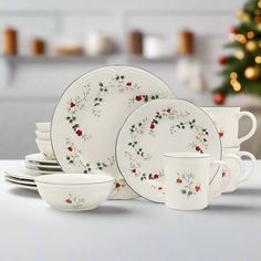 a white table topped with lots of plates and cups next to a christmas tree in the background