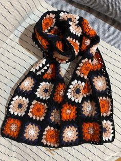 an orange and black crocheted scarf laying on top of a bed