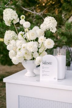 white flowers are in a vase on top of a table with a menu and candle