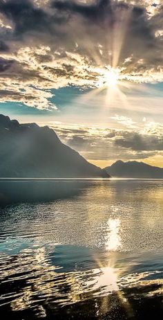 the sun shines brightly through the clouds over water with mountains in the back ground