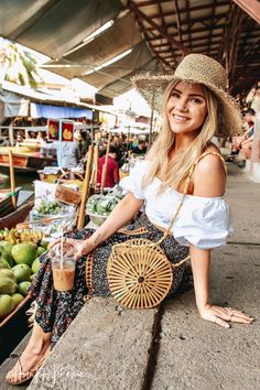 a woman in a straw hat is sitting on a ledge with a basket and drink