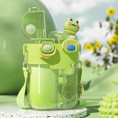 a green toy camera sitting on top of a white table next to a vase with yellow flowers