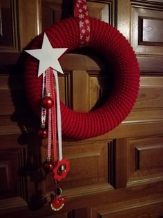 a red knitted wreath with white star hanging from it's side on a wooden door