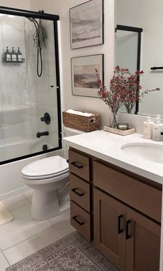 a white toilet sitting next to a bathroom sink under a mirror and framed pictures on the wall