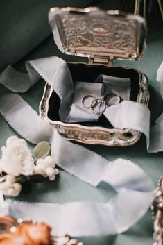 two wedding rings are placed in an open silver box on the table next to flowers