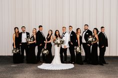 a group of people standing next to each other in front of a white wall holding bouquets