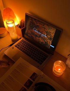 an open laptop computer sitting on top of a desk next to a candle and book